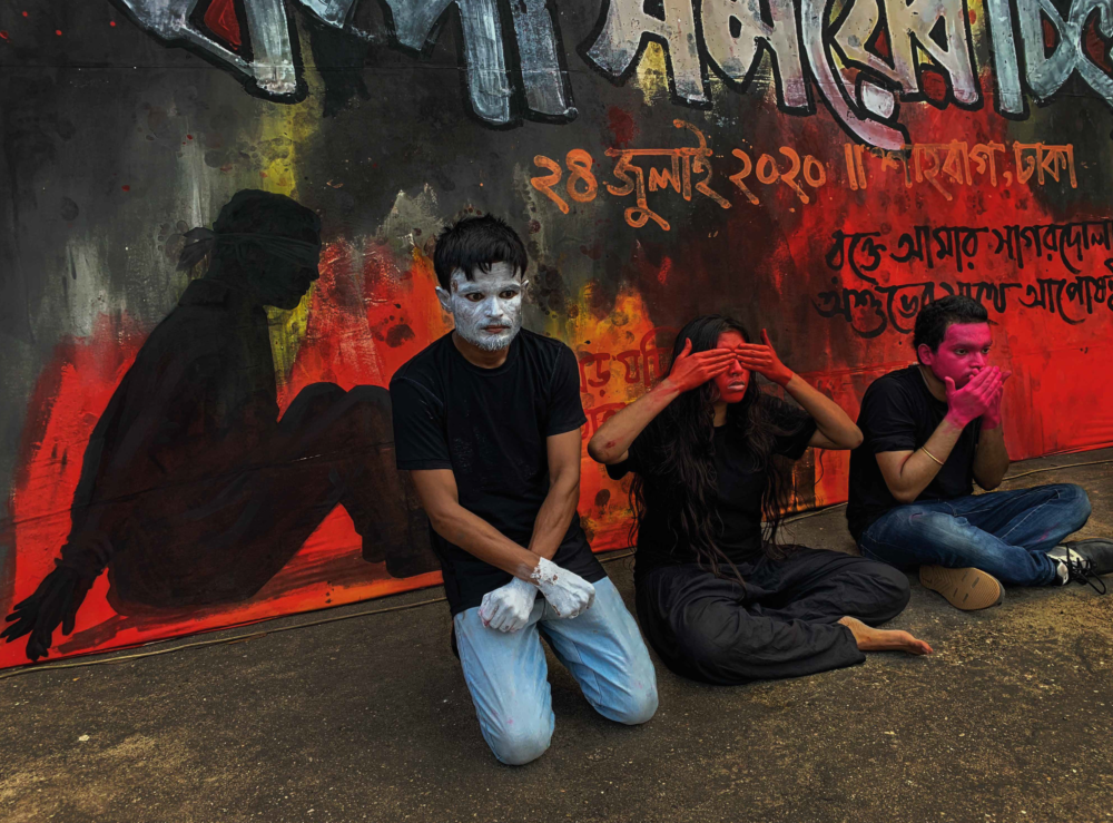 three artists seated in protest in front of a graffiti wall
