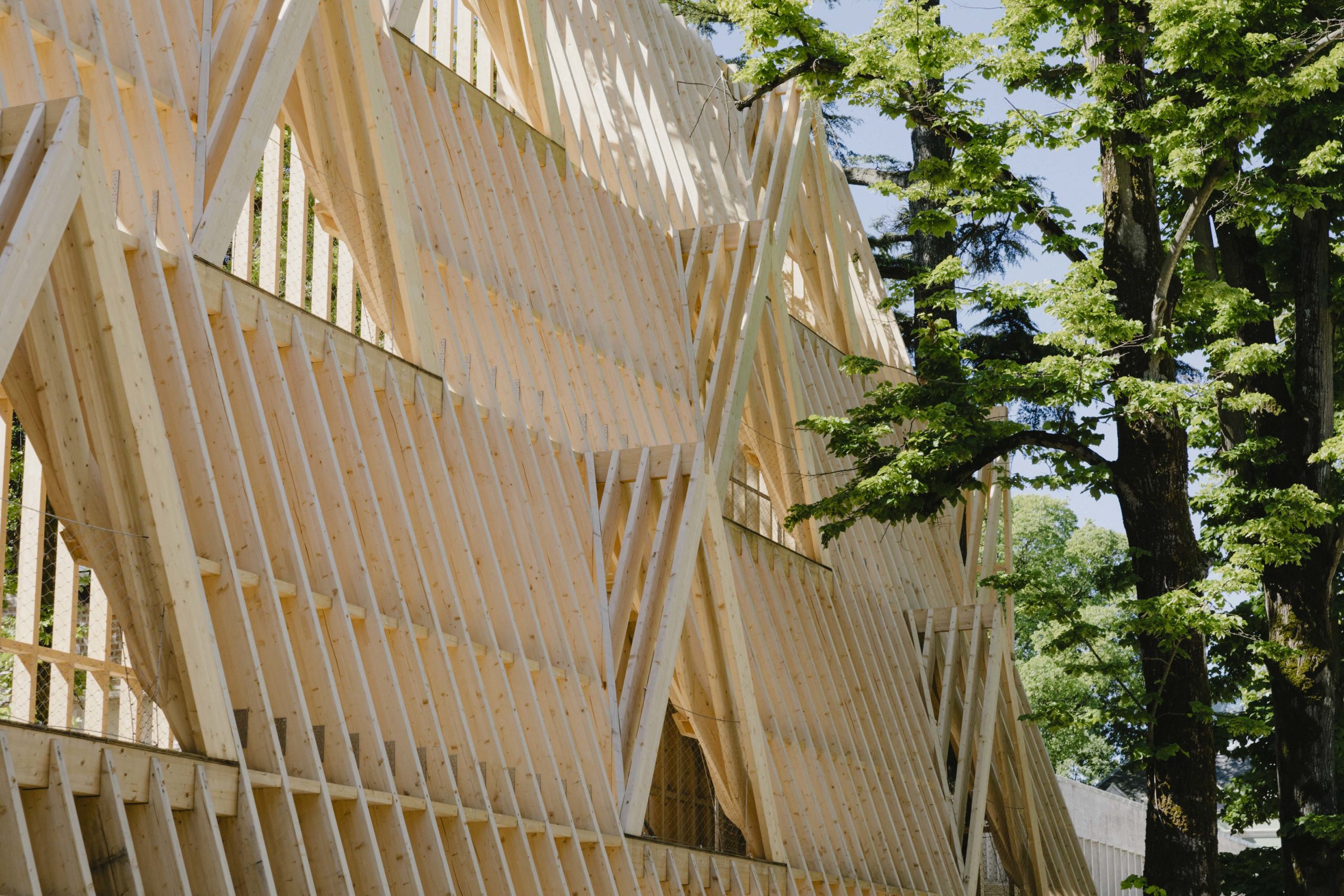 Peaked roof structure made of 2 by 4 wood with trees next to it